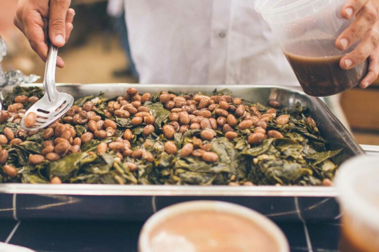 Braised Collard Greens with cranberry beans being scooped by a chef.