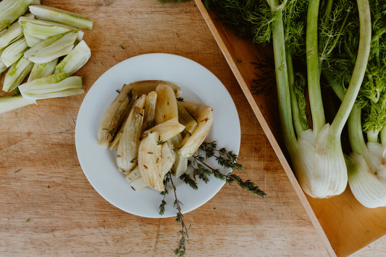 Plate of braised fennel next to fresh fennel.