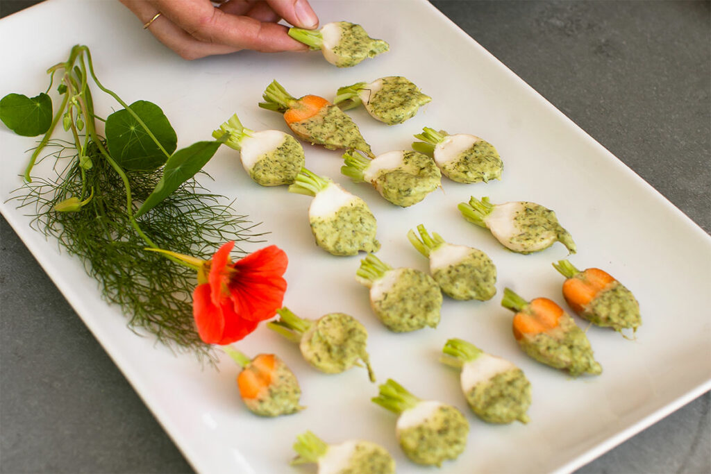 Chilled baby veg with herbed butter on platter with nasturtium as decor.