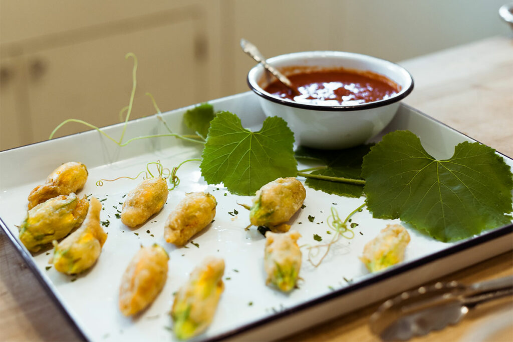 Stuffed Tempura Squash Blossoms on a platter with dipping sauce.
