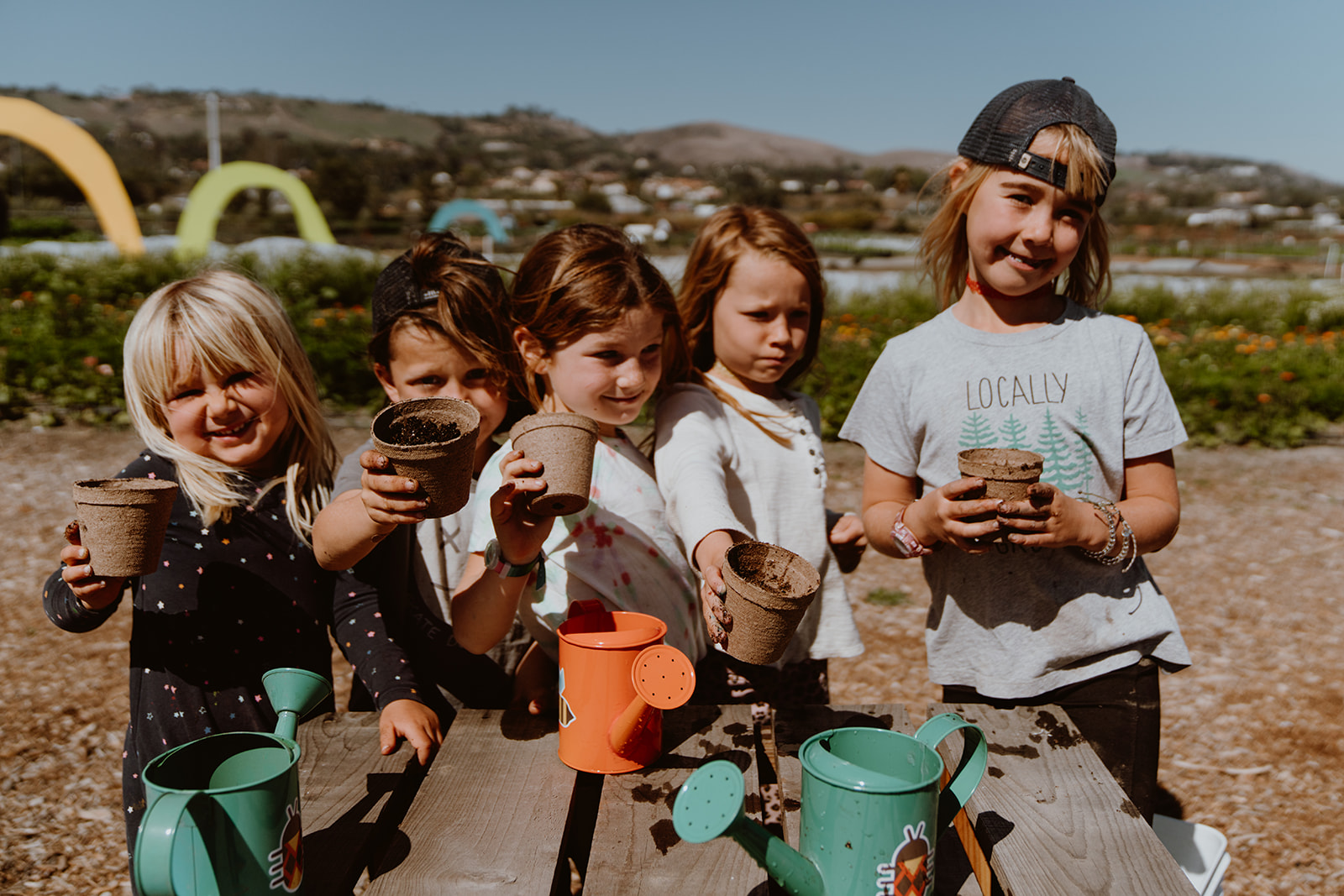 5 children stand at the end of a picnic table holding pots.