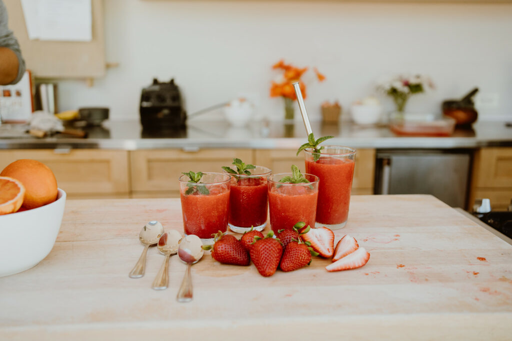 Strawberry & Blood Orange Granita on a wooden countertop in cups with spoons and whole strawberries.