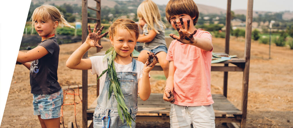 Three happy children show their dirty hands from planting in the fields.