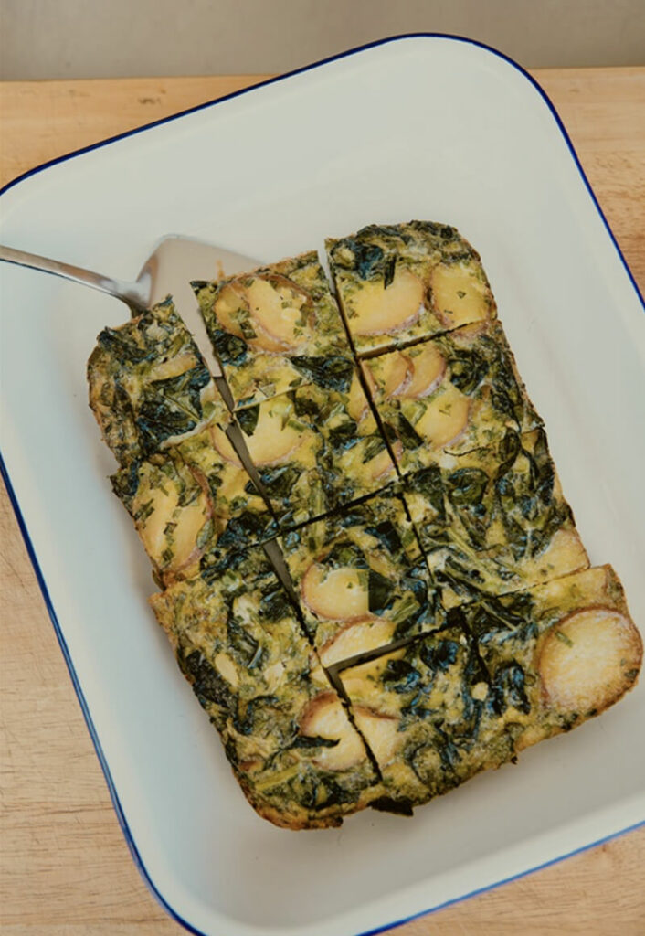 Baked spinach frittata in a white dish with blue rim.