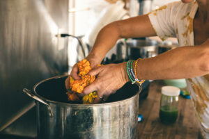 hands pouring marigold flowers into a pot for natural dye