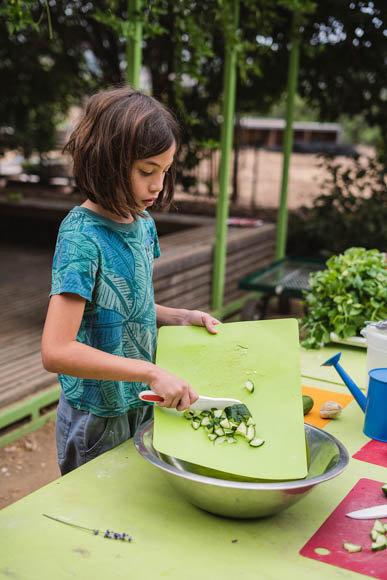 young child scrapping cut cucumbers into a bowl