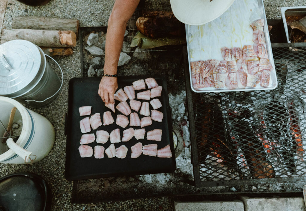 Top down photo of a chef preparing fish over an open wood fire.