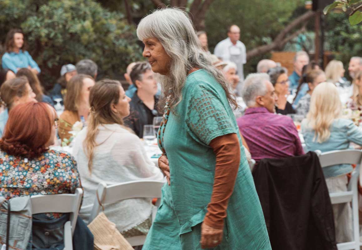 Person in a turquoise dress walks past the long table of attendees.