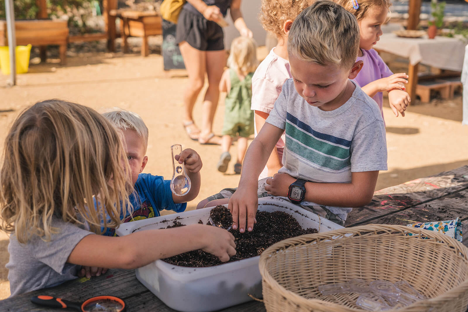 three kids gathered around a tub of dirt exploring what's inside