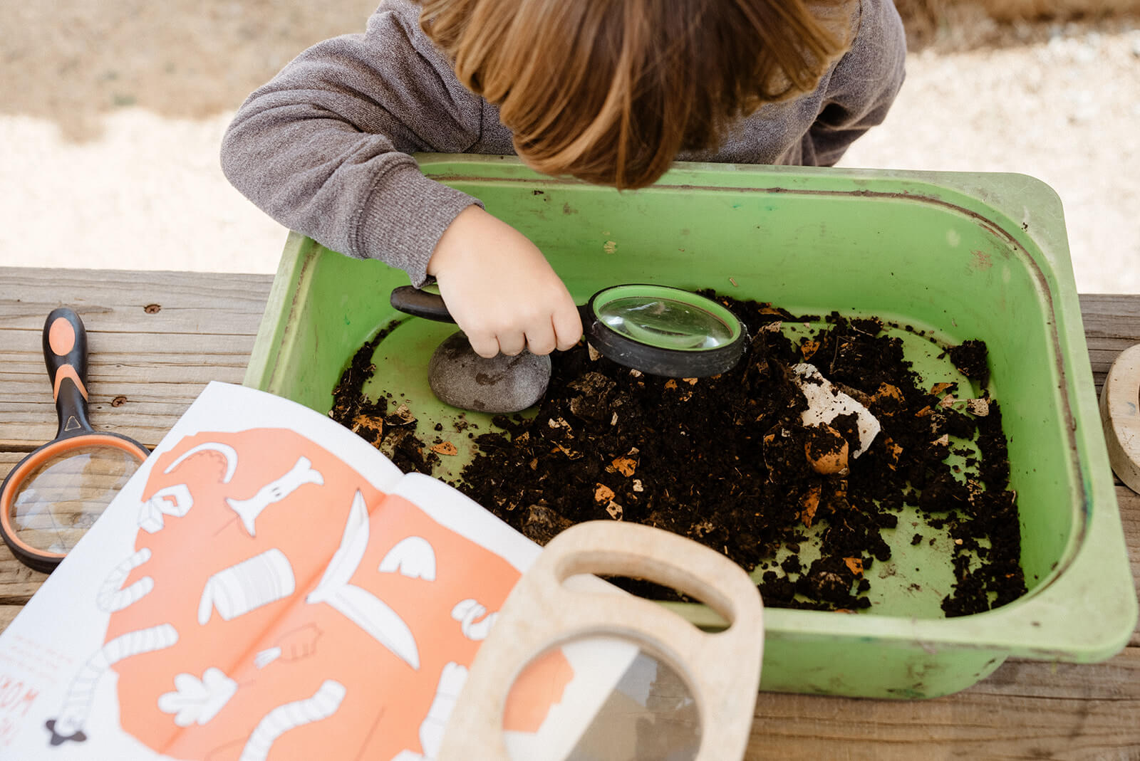 Child playing with magnifying glass in a green tray of dirt