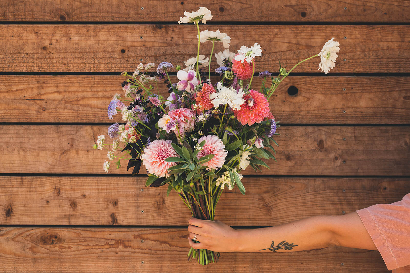 hand stretched out holding a bouquet of flowers in front of a wood door