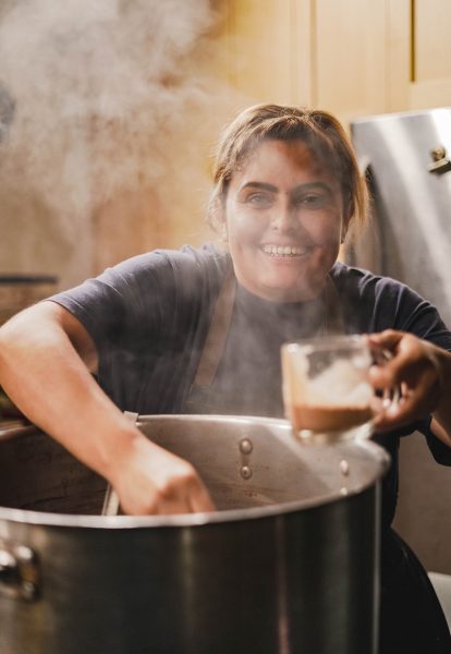 Person smiles as the serve beans out of a large pot.